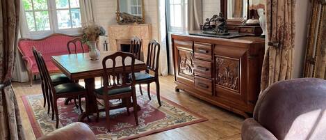 A traditional room with a wooden dining table, chairs, a sofa, and a cabinet with a mirror.
