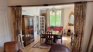 A traditional living room with a wooden dining table, two leather armchairs, a chandelier, and a fireplace.