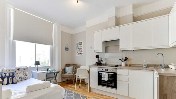 A compact, modern apartment with a kitchenette, a dining area, and a bedroom.