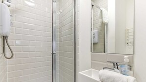 A modern bathroom with a glass shower enclosure, white tiled walls, a white sink with a towel, and a mirror.