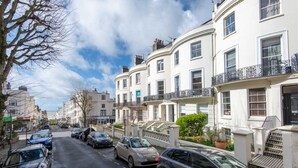 A street lined with white terraced houses, parked cars, and a clear sky.
