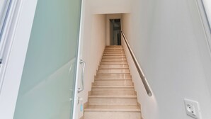 Eine Treppe mit Handlauf, eine Tür links und ein Lichtschalter an der Wand.