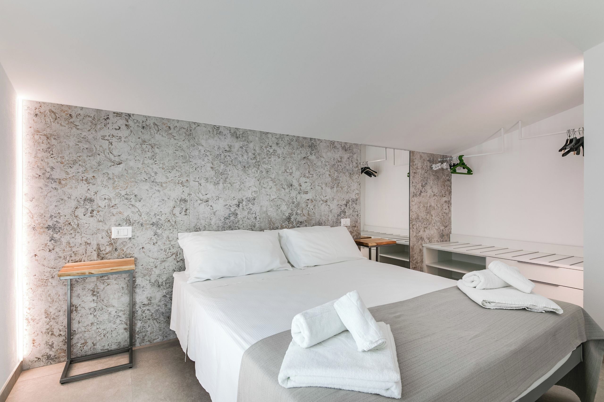 Een moderne hotelkamer met een groot bed, een houten nachtkastje, een spiegel en een handdoek op het bed.