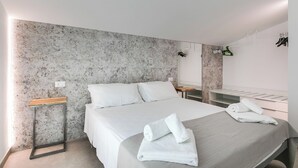 Ein modernes Hotelzimmer mit einem großen Bett, einem Holfnachtkästchen, einem Spiegel und einem Handtuch auf dem Bett.