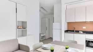 Eine moderne, kompakte Küche mit weißen Schränken, einem eingebauten Backofen und einer kleinen Essecke mit Tisch und Stühlen.