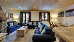 A cozy living room with a stone fireplace, a blue sofa set, a wooden coffee table, and a dining table with chairs. - Joli Chalet, Vieux Village (Val-d'Isère)