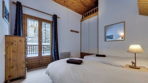 A bedroom with two beds, a wooden wardrobe, a balcony with a view of snow-covered trees, and a framed picture on the wall. - Joli Chalet, Vieux Village (Val-d'Isère)