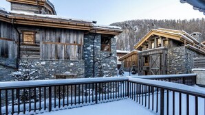 A snow-covered wooden building with stone walls, a balcony with a metal railing, and a view of a snowy forest. - Joli Chalet, Vieux Village (Val-d'Isère)
