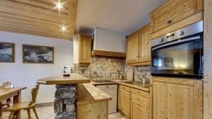 A kitchen with wooden cabinets, a stone island, a dishwasher, and a built-in oven. - Joli Chalet, Vieux Village (Val-d'Isère)