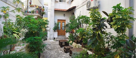Un patio estrecho con un sendero adoquinado, bancos de madera y plantas en macetas.