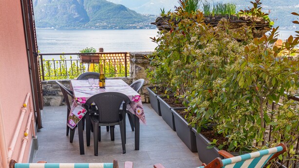 Un patio al aire libre con una mesa y sillas, una hamaca a rayas y vistas a un lago y montañas.