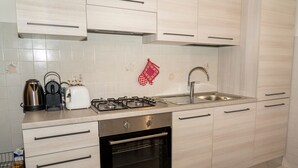 Una cocina moderna con armarios de madera clara, un lavamanos de acero inoxidable, una estufa a gas y un horno empotrado.