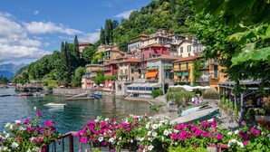 Un pintoresco pueblo frente al agua, con edificios de colores, un muelle para barcos y abundante vegetación.