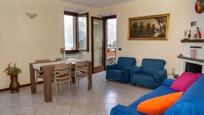 Una sala de estar con comedor, sofás azules, un cuadro y vistas al exterior.