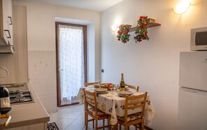 A kitchen with a dining table set for two, a stove, and a refrigerator. - Rosa House Varenna Apartment with a view of Lake Como (Varenna)