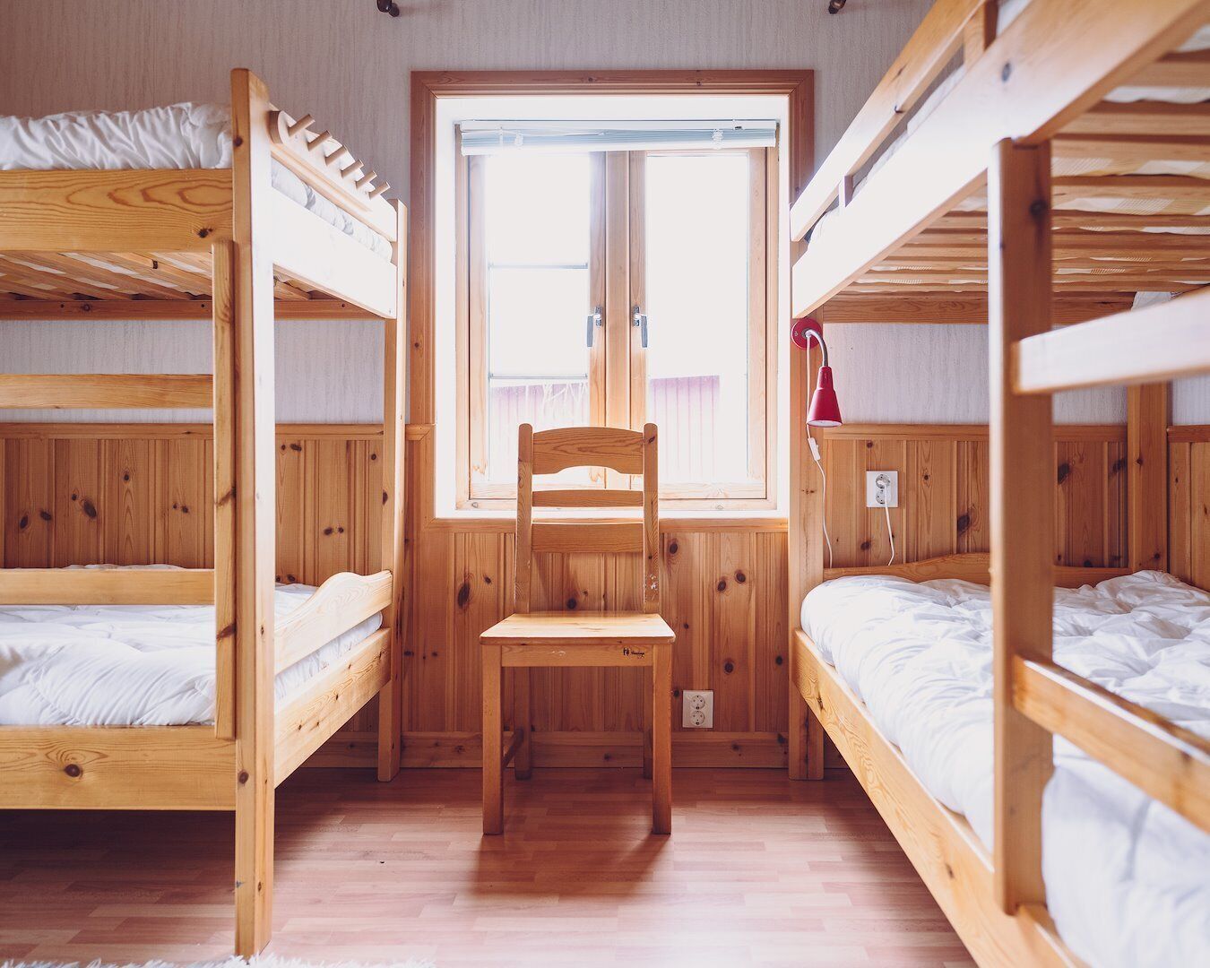 Un dormitorio con literas, una silla de madera y una ventana.