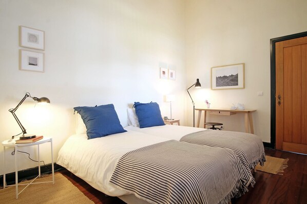 Une chambre à coucher avec un lit, deux tables de chevet, un bureau et une porte.
