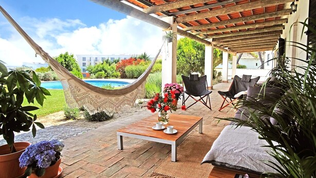 Un patio techado con una hamaca, una mesa de madera con tazas y sillas.