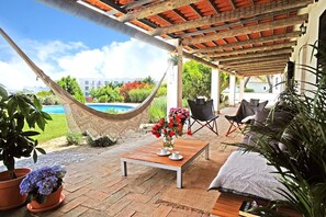Un patio techado con una hamaca, una mesa de madera con tazas y sillas.