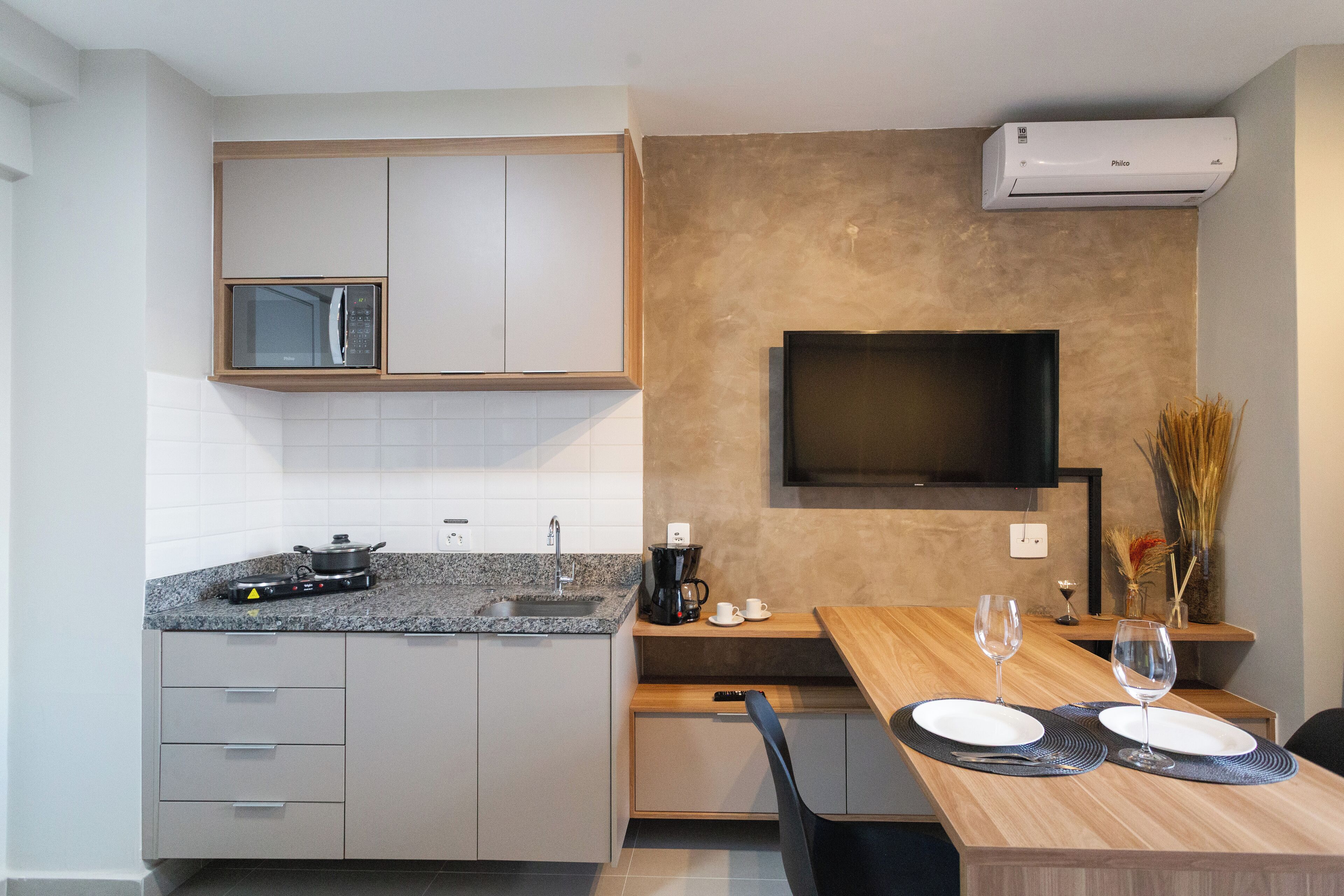 A modern kitchen with a microwave, stove, and sink. There is a dining table with two wine glasses and plates.