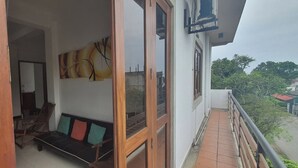 Un balcon avec un plancher en bois, un canapé noir agrémenté de coussins colorés et un tableau accroché au mur.
