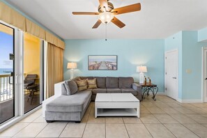 Ein Wohnzimmer mit einer Couch, einem Couchtisch, einem Deckenventilator und Blick auf den Ozean durch eine Schiebetür.
