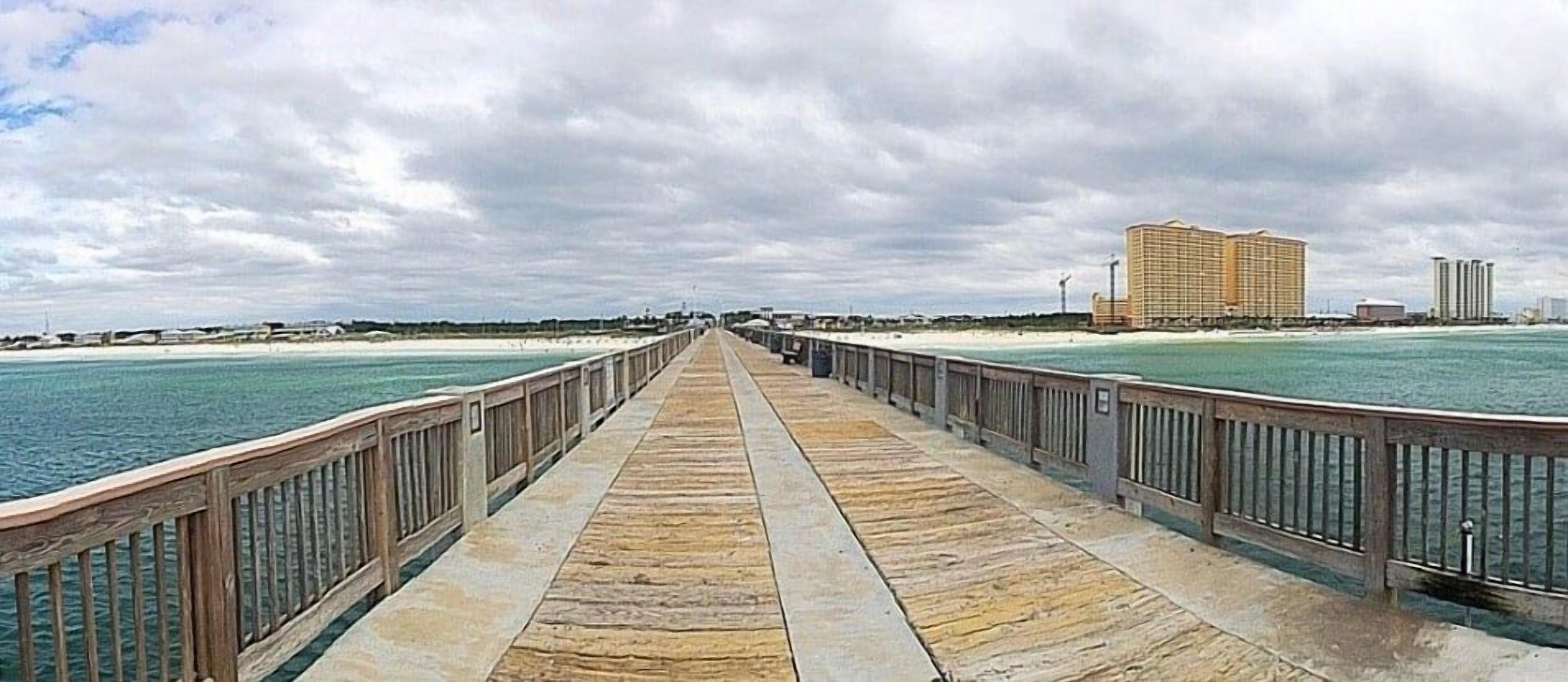 En träpromenad som leder till en strand, med ett hotell och höga byggnader i bakgrunden.
