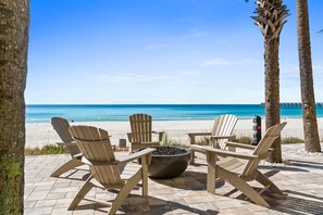 Un espacio de descanso frente a la playa con sillas tipo Adirondack y una hoguera, con vistas al océano azul y transparente.