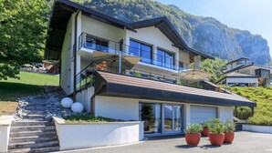 A modern two-story house with a balcony, large windows, and a mountain backdrop. - Le Clos du Lac: Villa with lake view (Veyrier-du-Lac)