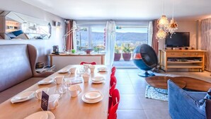 A modern living room with a dining area, a large window with a view, and a TV. - Le Clos du Lac: Villa with lake view (Veyrier-du-Lac)