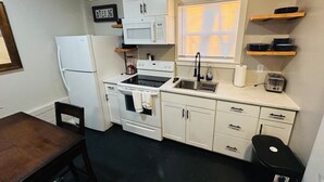 A compact kitchen with white appliances, a sink, and a window with blinds. - Madison gate studio (Goldsboro)