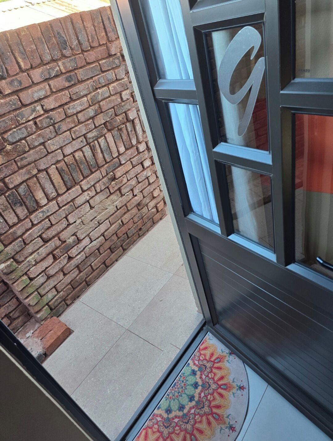 A brick wall adjacent to a glass door with a large letter 'G' on it.