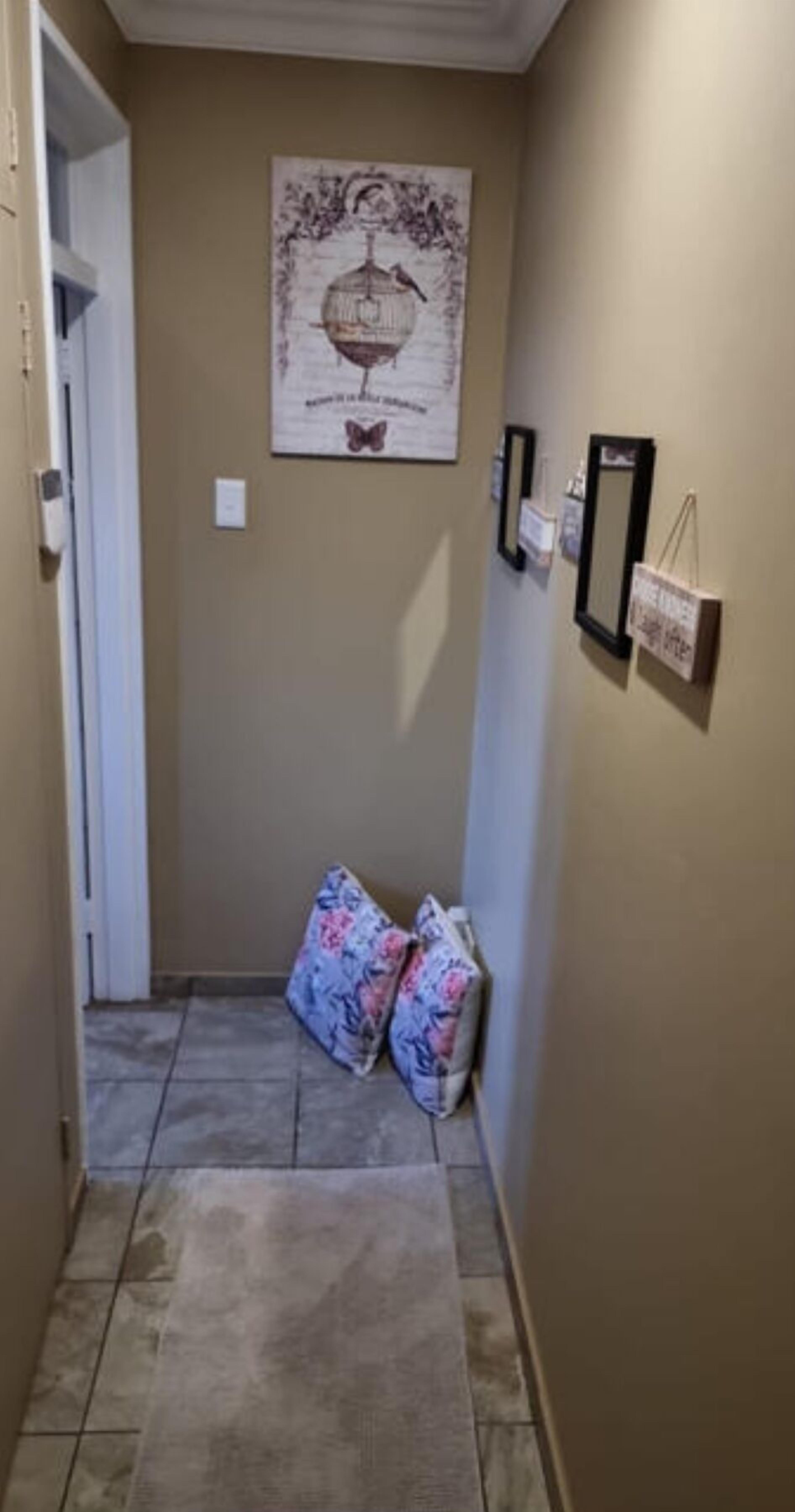 A narrow hallway with a tiled floor, a door on the left, and a wall with a framed picture and two small framed items.