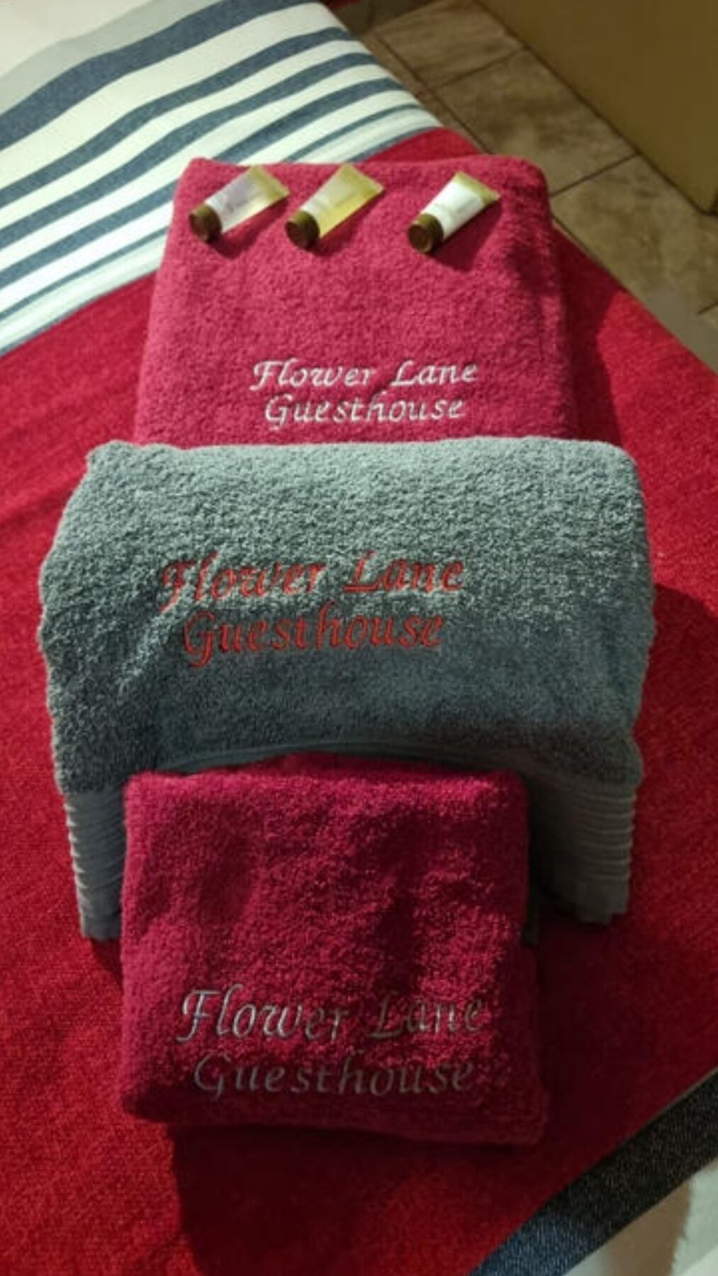 En hög med handdukar med broderad text som anger att det är ett gästhus som heter ”Flower Lane Guesthouse”.