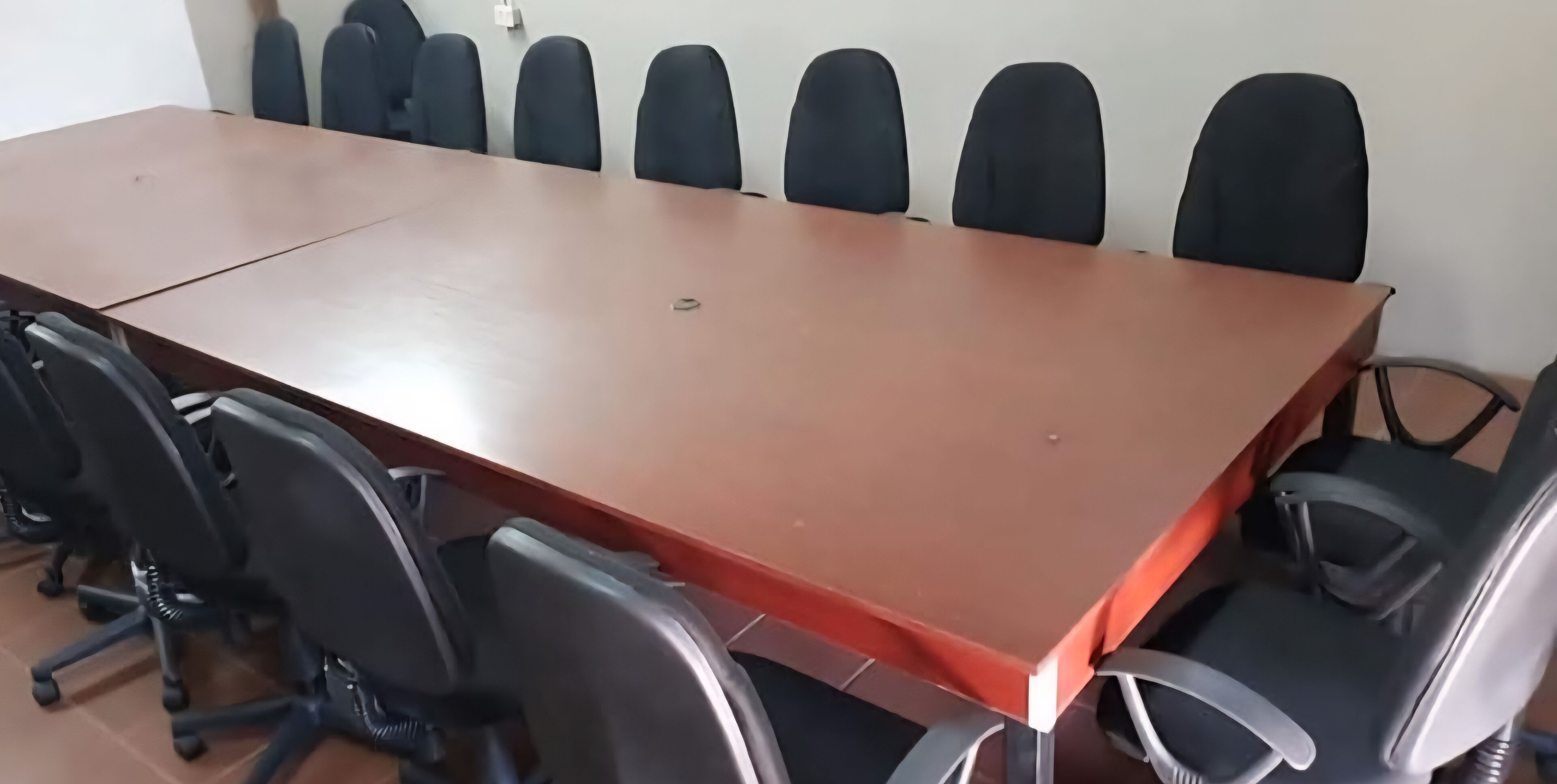 Une salle de conférence avec une longue table et plusieurs chaises de bureau noires.