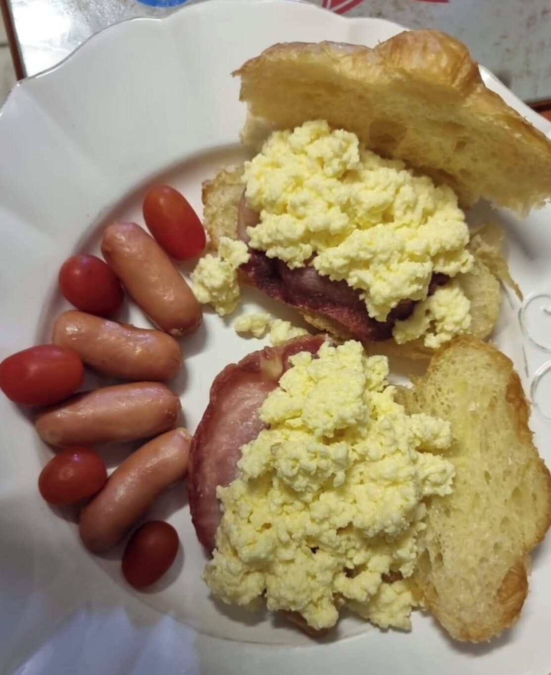 A plate with scrambled eggs, bacon, sausages, and tomatoes.