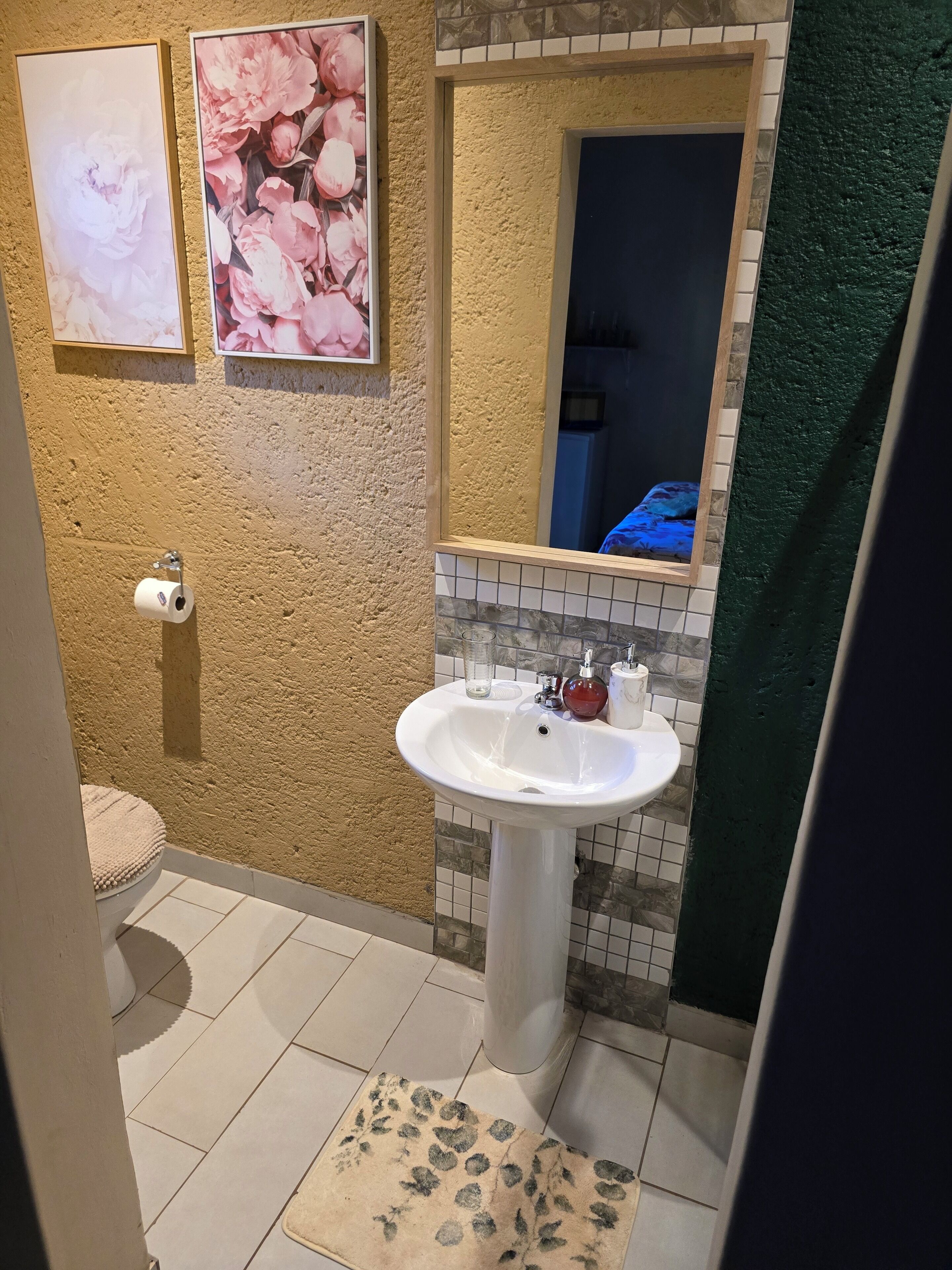 A bathroom with a white sink, a toilet, and a shower area. There are two framed floral pictures on the wall.