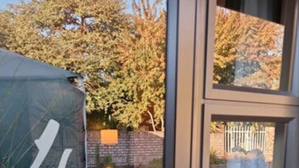 A glass door with a number '4' sticker, a small garden area with plants and a brick wall in the background. - Flower Lane Guesthouse  (Kathu)