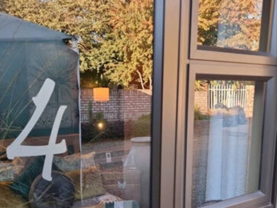 Uma porta de vidro com uma etiqueta com o número '4', uma pequena área de jardim com plantas e um muro de tijolos ao fundo.