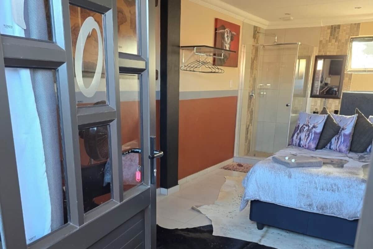 Habitación de hotel con cama, un espejo grande, zona de ducha y vistas al exterior.