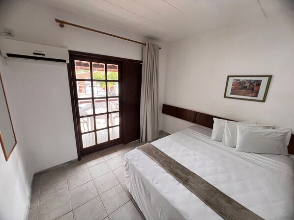 Quarto de hotel com cama, janela com cortinas, ar condicionado fixado na parede e quadro emoldurado.