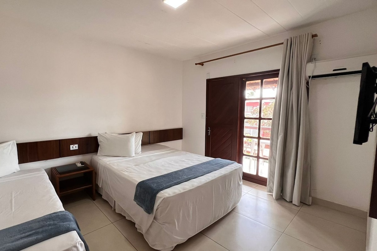 Une chambre d’hôtel avec deux lits, une petite table de chevet avec une lampe, une fenêtre avec des rideaux et une porte donnant sur l’extérieur.