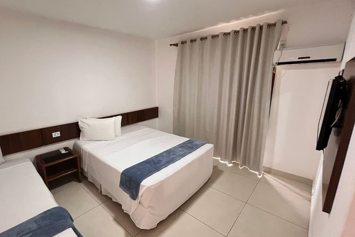 A hotel room with two beds, a nightstand, a wardrobe, and a window with curtains.