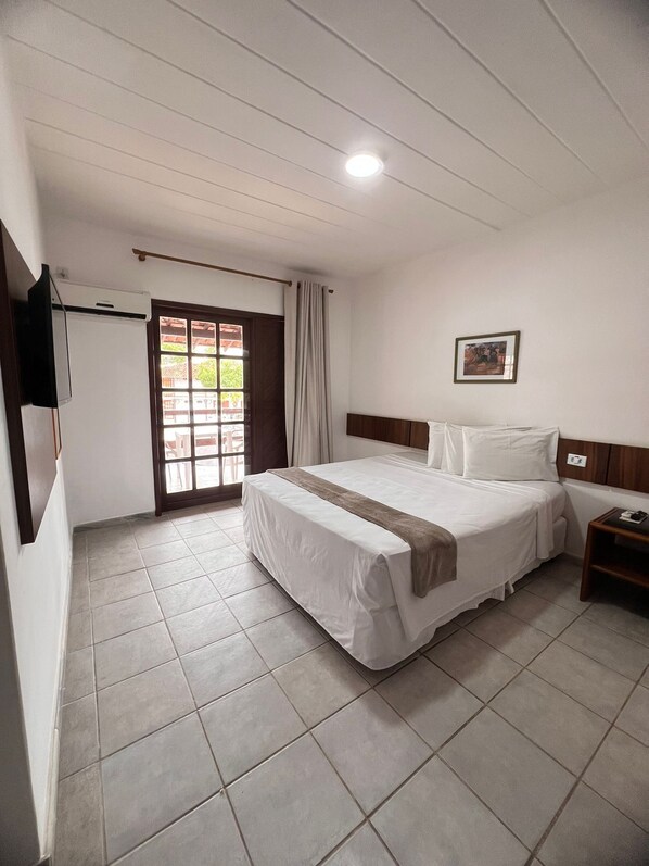 Une chambre d’hôtel avec un lit, une télévision, une fenêtre avec des rideaux et un tableau au mur.