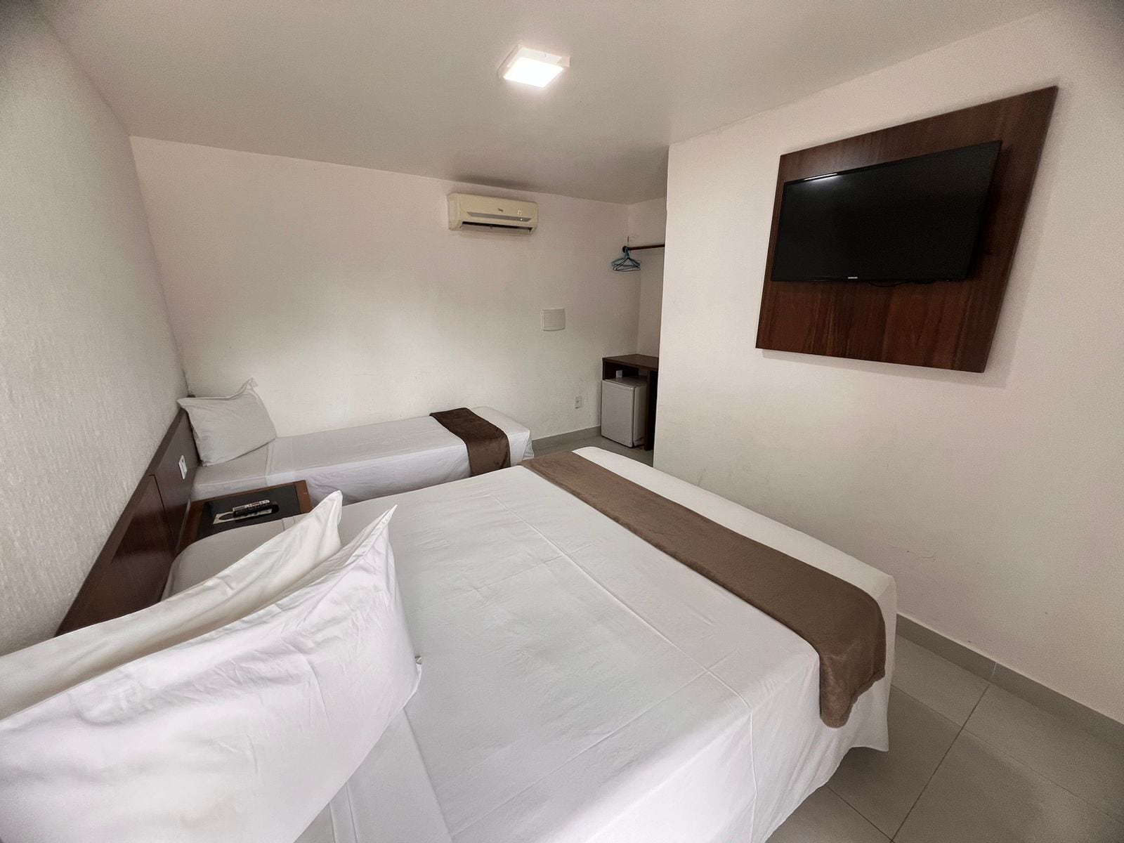 A hotel room with two single beds, a TV mounted on the wall, a small desk, and a mini-fridge.