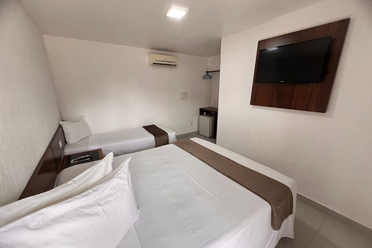 A hotel room with two single beds, a TV mounted on the wall, a small desk, and a mini-fridge.
