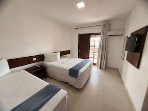 Une chambre d’hôtel avec deux lits, une tête de lit en bois, une table de chevet, un téléviseur fixé au mur et une fenêtre avec des rideaux.