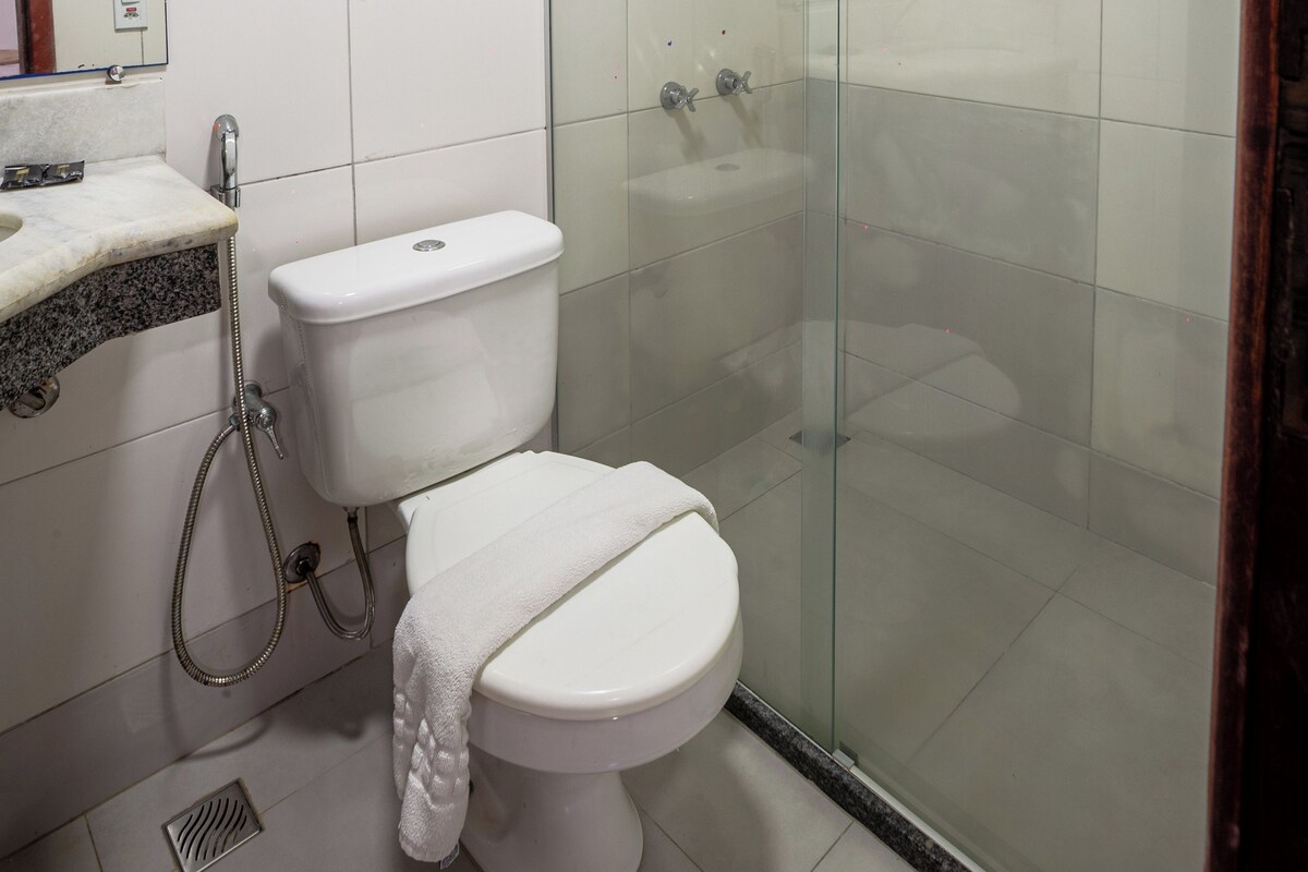 Um banheiro moderno com chuveiro em box de vidro, vaso sanitário branco e pia de mármore.