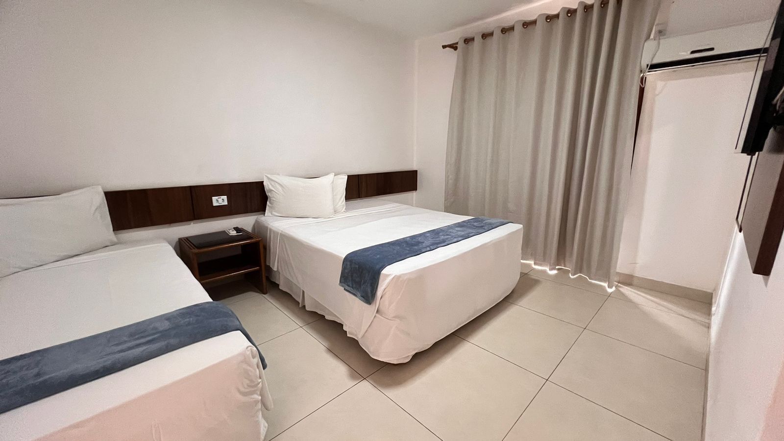 A hotel room with two beds, a nightstand, a wardrobe, and a curtain.