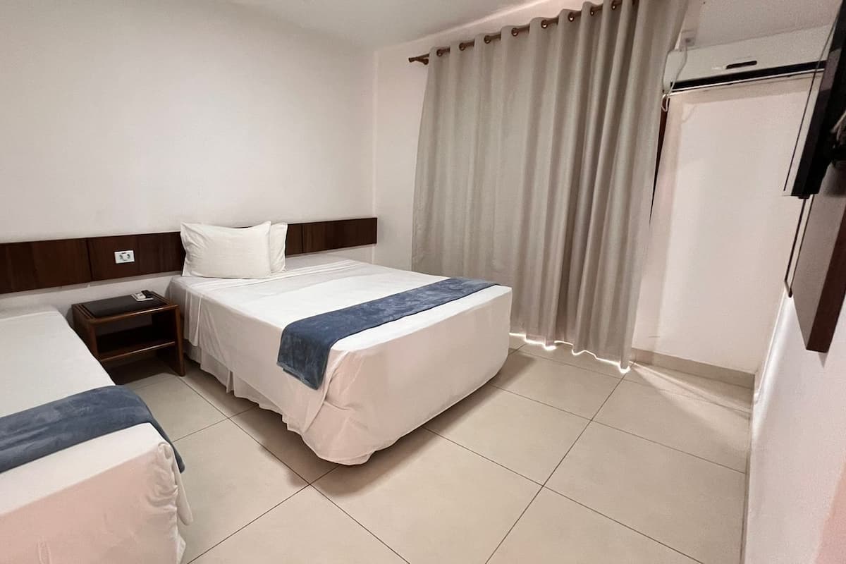 A hotel room with two beds, a nightstand, a wardrobe, and a curtain.